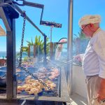 Chef cooking meeting on an outdoor barbecue with ocean in background.